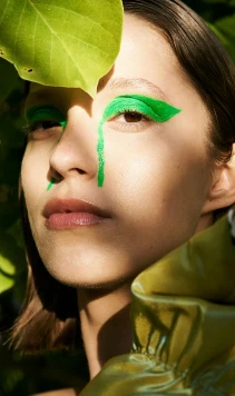 A person with green make-up stood amongst leaves.