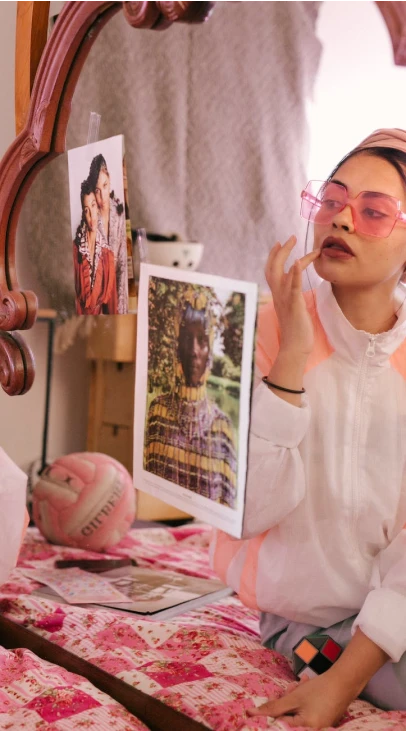 A person with pink glasses applying makeup at a vanity table.