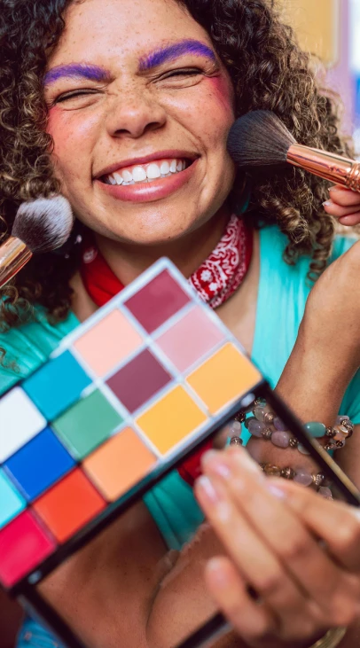 A person holding brushers and a palette of makeup.