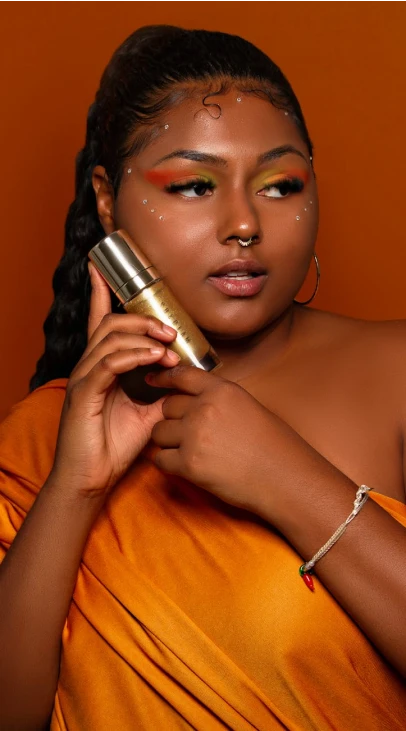 A person in an orange dress holding a bottle of makeup to their face.