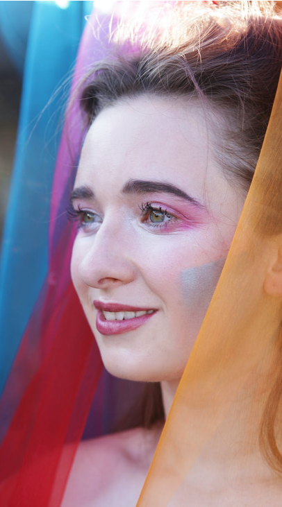 A person with multi-coloured makeup and multi-coloured veil.