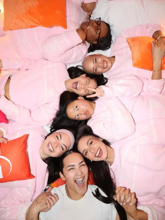 Creators posing together on a pink bed.
